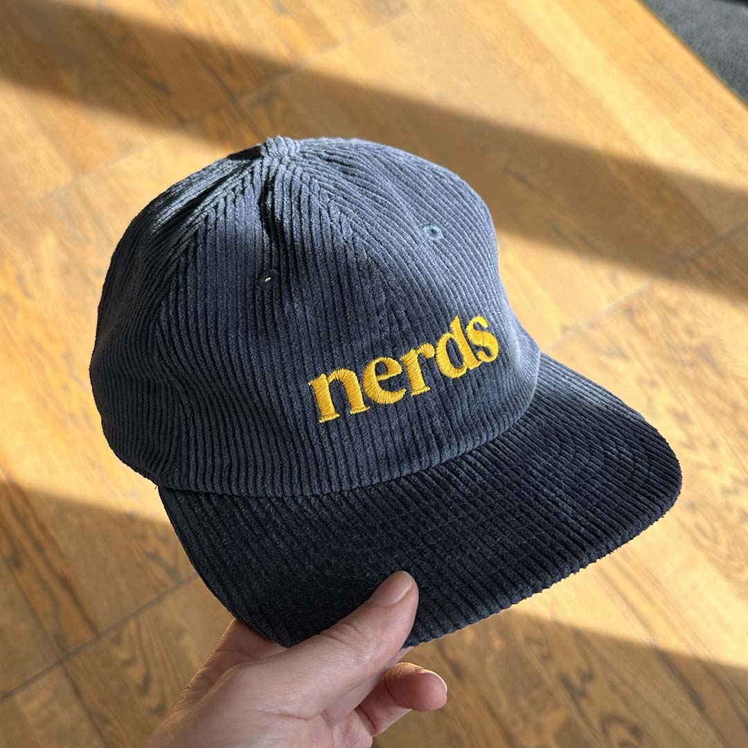 Navy blue cap with 'nerds' embroidery in yellow on a wooden surface