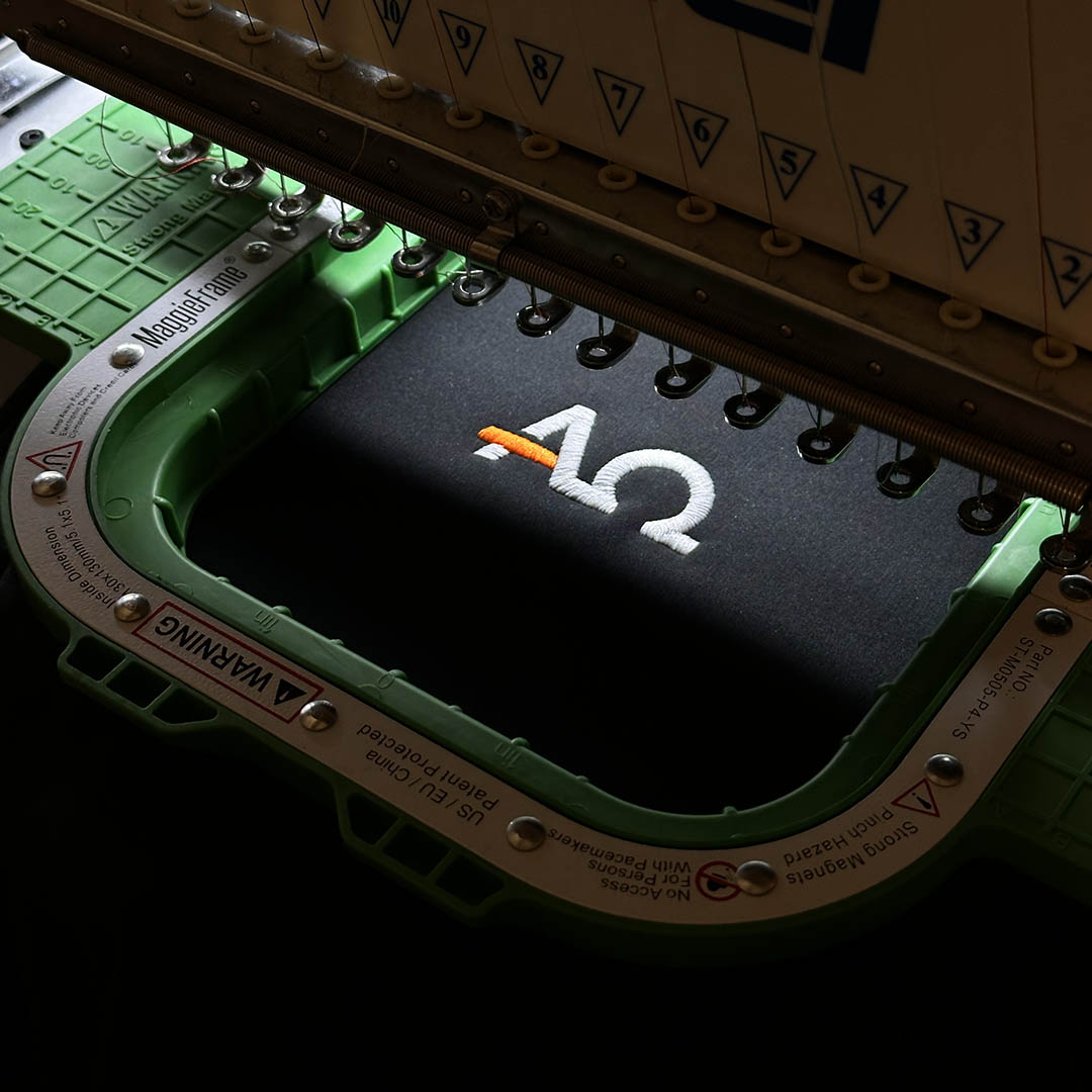 Close-up of an embroidery machine with a brand logo on a dark background