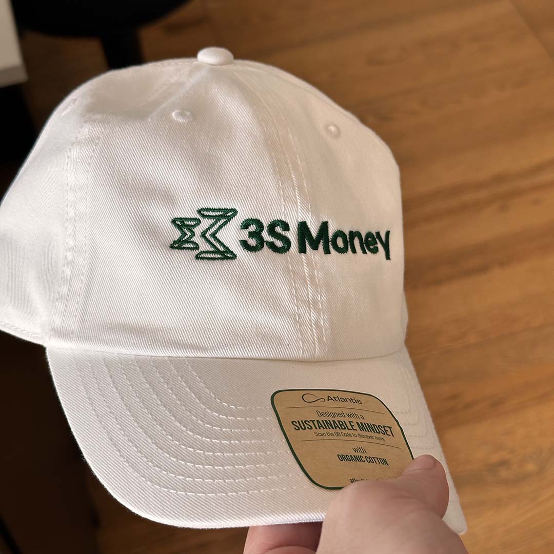 White cap with '3S Money' logo embroidery held by a hand on a wooden floor.
